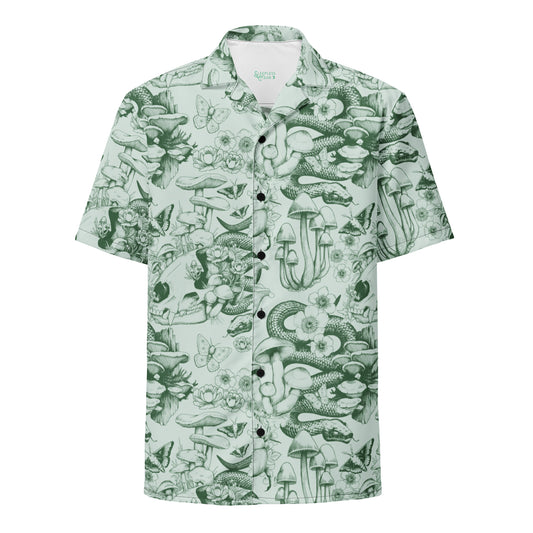 A flat-lay product photo of a short-sleeve, button-down Hawaiian-style shirt with an oversized fit. The shirt features an all-over, monochrome forest floor pattern in dark green ink over a light sage green background. The detailed illustration includes coiling snakes, clusters of tall mushrooms, animal skulls, butterflies, and small wildflowers. The shirt has black buttons down the center and a white inner collar showing a small green logo.A flat-lay product photo of a short-sleeve, button-down Hawaiian-sty