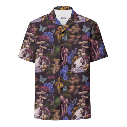 A flat-lay product photo of a short-sleeve, button-down Hawaiian-style shirt with an oversized fit. The shirt features an all-over, multi-colored forest floor pattern on a deep purple background. The detailed illustration includes animal skulls with wild mushrooms growing out of them, green beetles, coiling snakes, blue butterflies, and clusters of purple, pink, and blue flowers. The shirt has black buttons down the center and a white inner collar showing a small green logo.