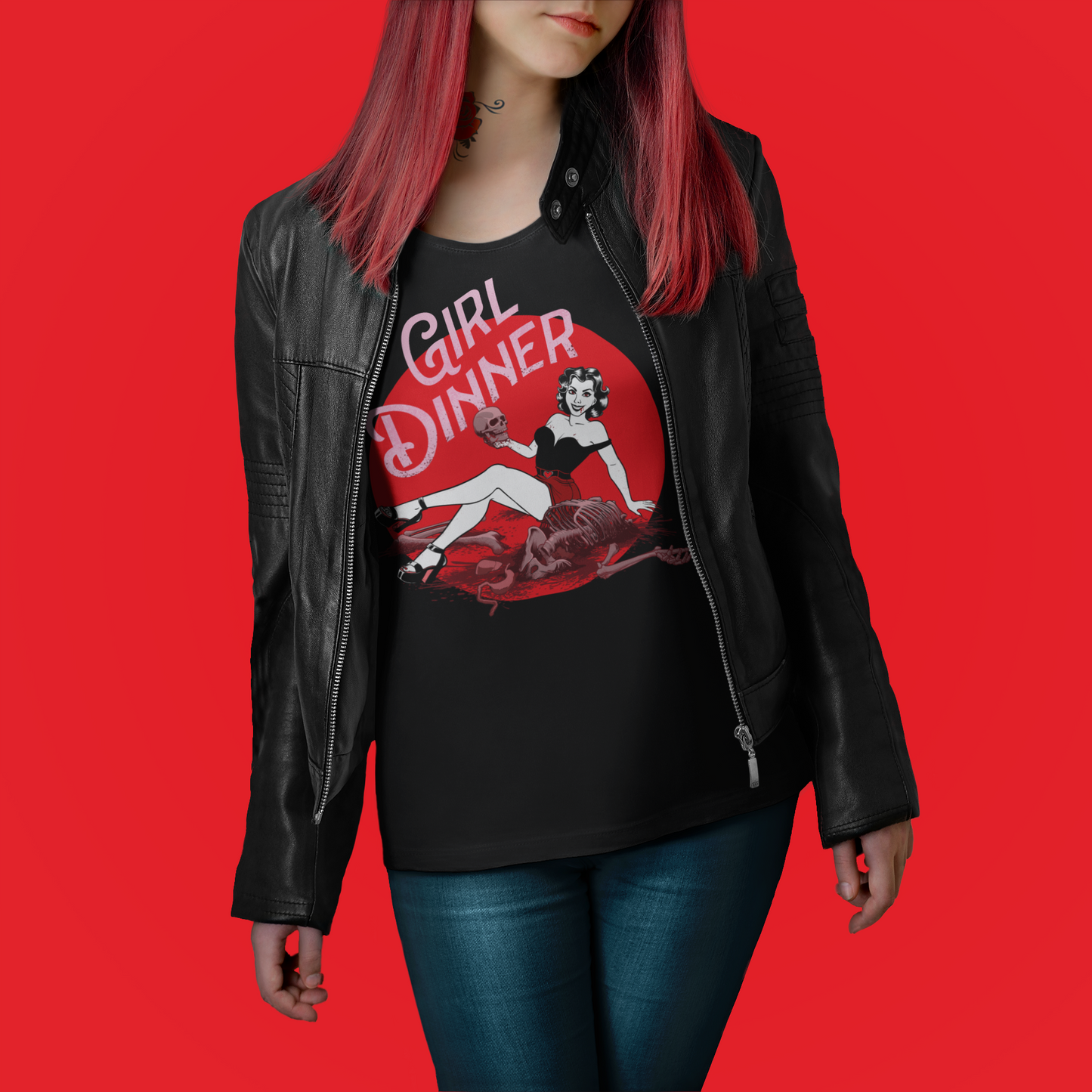 A woman wearing a black leather jacket over a black graphic t-shirt with a red and white 'Girl Dinner' pin-up illustration, paired with blue jeans, set against a solid red background.