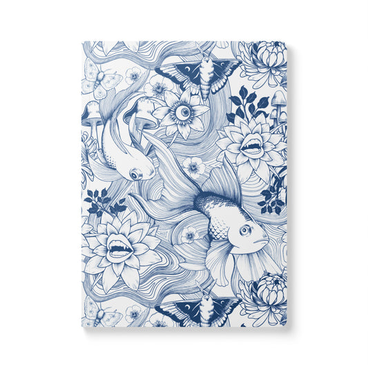 A front-facing view of a rectangular softcover journal with rounded corners, featuring a detailed dark blue ink illustration pattern on a white background. The surreal pattern includes large goldfish, moths, mushrooms, and whimsical blooming flowers with fanged teeth and human eyes.