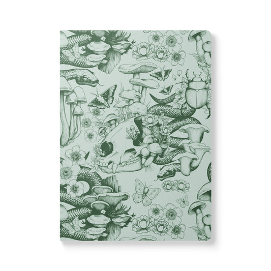 A front-facing view of a rectangular softcover journal with rounded corners, featuring a detailed dark olive green ink illustration pattern on a pale sage green background. The woodland-themed pattern includes an animal skull, snakes, a large beetle, butterflies, clusters of mushrooms, and blooming wildflowers.